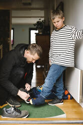 Vater, der seinem behinderten Sohn beim Anziehen der Schuhe hilft, steht an der Tür - MASF30438