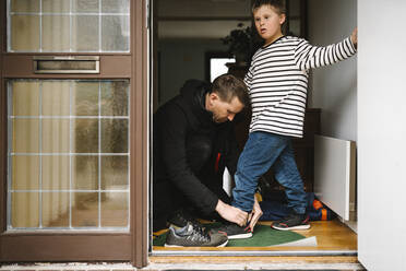 Vater, der seinem Sohn mit Down-Syndrom hilft, einen Schuh anzuziehen, steht an der Tür - MASF30440