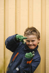 Porträt eines lächelnden Jungen mit Behinderung, der eine Fingerrahmengeste gegen die Wand macht - MASF30449