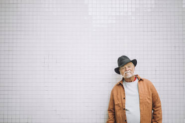 Porträt eines älteren Mannes mit Hut, der vor einer weißen Wand steht - MASF30465