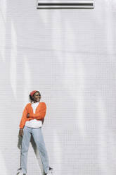 Lächelnde junge Frau, die wegschaut, während sie an einer weißen Wand steht - MASF30521
