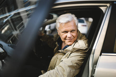 Lächelnder älterer Geschäftsmann, der die Tür öffnet, während er aus dem Auto aussteigt - MASF30608