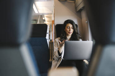 Businesswoman talking on video call through laptop while sitting in train - MASF30616