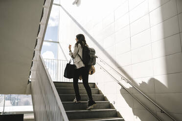 Rear view of businesswoman with backpack moving up on staircase at railroad station - MASF30622