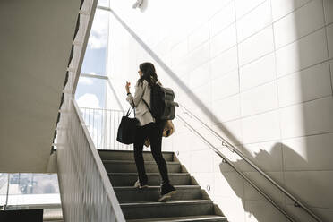 Rückansicht einer Geschäftsfrau mit Rucksack, die auf einer Treppe am Bahnhof nach oben geht - MASF30622