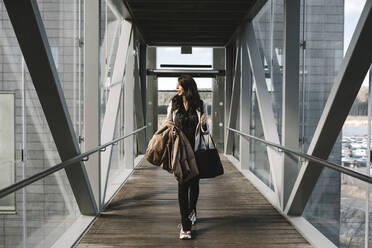Geschäftsfrau schaut weg und hält eine Tasche, während sie auf einer Fußgängerbrücke geht - MASF30623