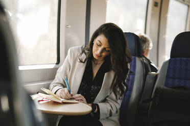 Businesswoman writing in diary while sitting by train window - MASF30624