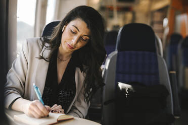 Geschäftsfrau mit langen Haaren, die im Zug sitzend in ihr Tagebuch schreibt - MASF30625