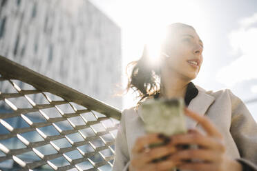 Niedriger Blickwinkel einer Geschäftsfrau, die ihr Smartphone an einem sonnigen Tag in der Hand hält - MASF30633