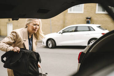 Blonde Geschäftsfrau lädt Gepäck in den Kofferraum eines Autos - MASF30652