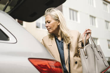 Niedriger Blickwinkel von blonden Geschäftsfrau hält Geldbörse, während stehend von Auto Kofferraum - MASF30654