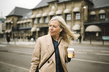 Businesswoman looking away while holding disposable coffee cup in city - MASF30671