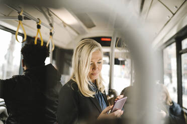 Female professional using smart phone while standing in bus - MASF30676