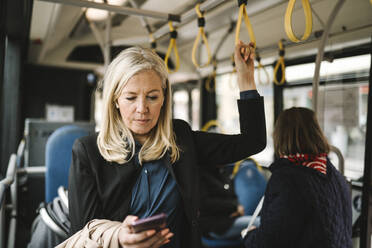 Businesswoman holding grab handle while using smart phone in bus - MASF30678