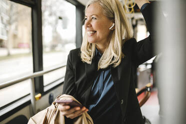 Glückliche Geschäftsfrau mit Smartphone auf Reisen im Bus - MASF30679