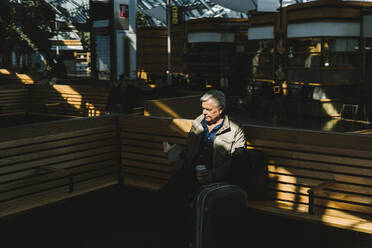 Geschäftsmann liest ein Buch, während er auf einer Bank am Bahnhof sitzt - MASF30687