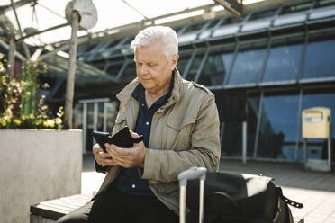 Geschäftsmann, der sein Smartphone benutzt, während er auf einer Bank am Bahnhof sitzt - MASF30692