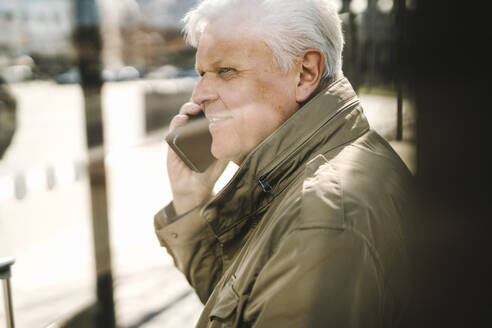 Seitenansicht eines älteren Geschäftsmannes, der mit einem Smartphone telefoniert, gesehen durch Glas - MASF30704