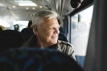 Happy businessman with gray hair looking through bus window - MASF30705