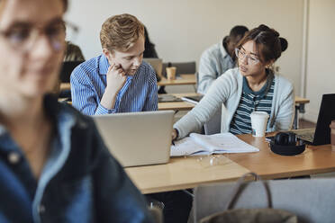 Eine Schülerin hilft einem männlichen Freund, während sie am Schreibtisch im Klassenzimmer sitzt - MASF30712