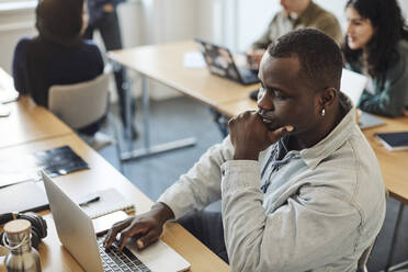 High angle view of thoughtful male student using laptop in classroom - MASF30720