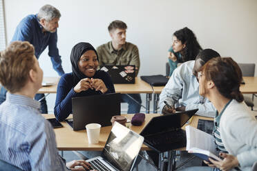 Lächelnde Studentin, die im Klassenzimmer mit Freunden diskutiert - MASF30724