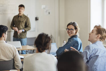 Lächelnde Studentin, die ihren Freund während einer Vorlesung im Klassenzimmer anschaut - MASF30730