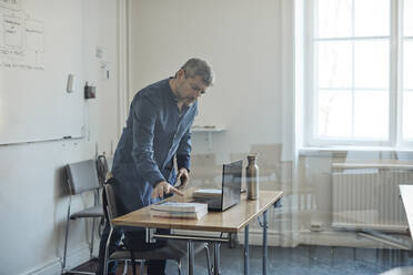 Männlicher Lehrer ordnet den Schreibtisch im Klassenzimmer einer Universität - MASF30746