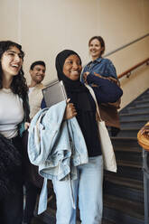 Lächelnde Freundinnen stehen in der Nähe einer Treppe in der Universität - MASF30758