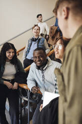 Glückliche junge gemischtrassige Studenten, die sich im Treppenhaus einer Universität vergnügen - MASF30761