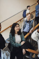 Lächelnde Studentin mit Freunden, die sich im Treppenhaus vergnügen - MASF30762