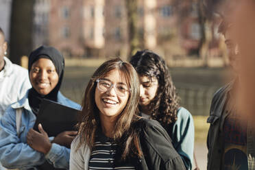 Portrait of smiling young female student with friends at university campus on sunny day - MASF30778