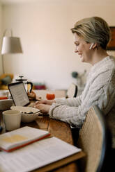 Seitenansicht einer lesbischen Geschäftsfrau mit Laptop am Esstisch sitzend - MASF30787