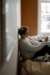 Depressive junge lesbische Frau mit Schwangerschaftstestergebnissen, die zu Hause auf dem Bett sitzt - MASF30799