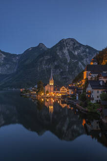 Österreich, Oberösterreich, Hallstatt, Blick auf den Ort am Seeufer in der Abenddämmerung mit beleuchteter Kirche im Hintergrund - RUEF03678