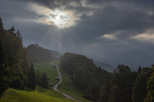 Deutschland, Bayern, Wamberg, Bewölkter Himmel über einer kleinen Straße, die zu einem abgelegenen Dorf im Wettersteingebirge führt - RUEF03679