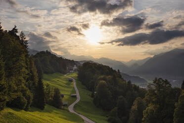 Deutschland, Bayern, Wamberg, Sonnenuntergang über einer kleinen Straße, die zu einem abgelegenen Dorf im Wettersteingebirge führt - RUEF03683