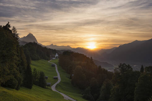 Deutschland, Bayern, Wamberg, Sonnenuntergang über einer kleinen Straße, die zu einem abgelegenen Dorf im Wettersteingebirge führt - RUEF03684
