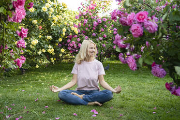 Smiling woman practicing yoga amidst rose plants in garden - SVKF00231