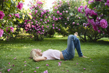 Woman with hands behind head lying on grass at garden - SVKF00232