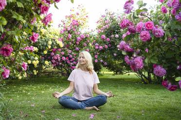Frau mit geschlossenen Augen meditiert inmitten eines Rosengartens - SVKF00235