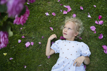 Thoughtful cute girl lying on grass at rose garden - SVKF00236