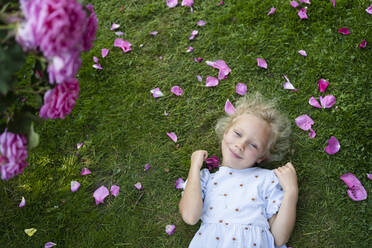 Smiling girl holding rose lying on grass at garden - SVKF00237