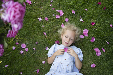 Girl with eyes closed holding a rose petal resting by lying on grass - SVKF00238