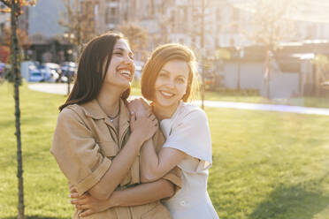 Happy woman hugging cheerful friend at park on sunny day - OMIF00817