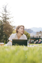 Woman with laptop lying at park - OMIF00826