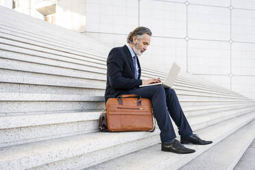 Mature businessman using laptop sitting on steps - OIPF01947