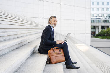 Smiling businessman with laptop sitting on steps - OIPF01950