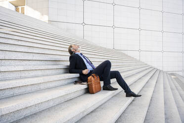 Älterer Geschäftsmann sitzt mit Tasche entspannt auf Stufen - OIPF01963