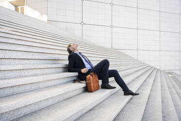 Mature businessman sitting by bag relaxing on steps - OIPF01963